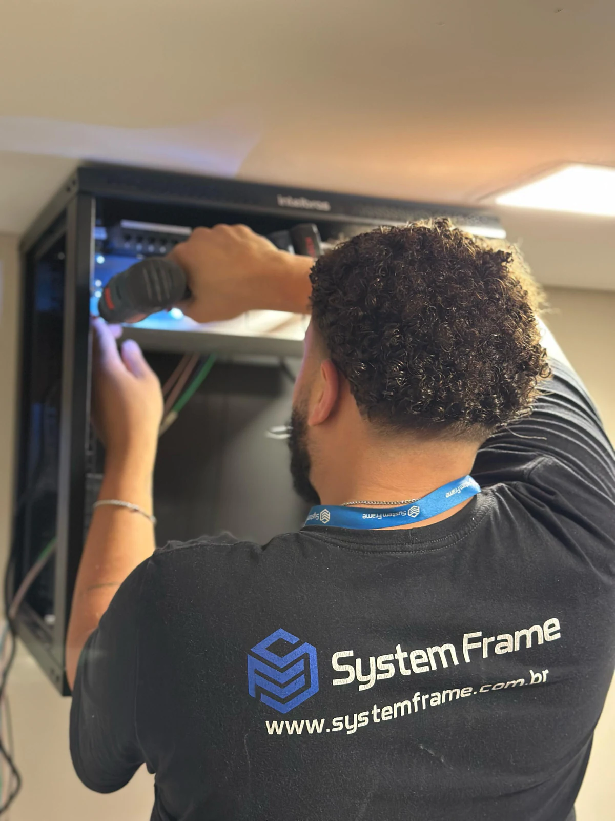 Técnico de costas usando uma ferramenta junto ao equipamento de rede no rack.