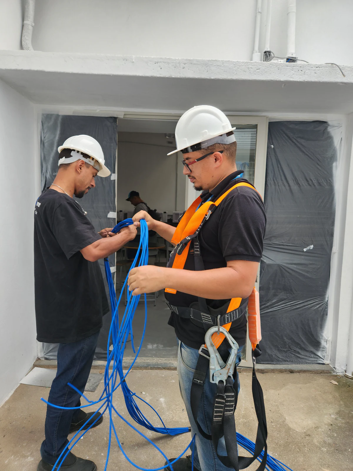 Técnicos de capacete preparando cabos de rede em ambiente de obra.