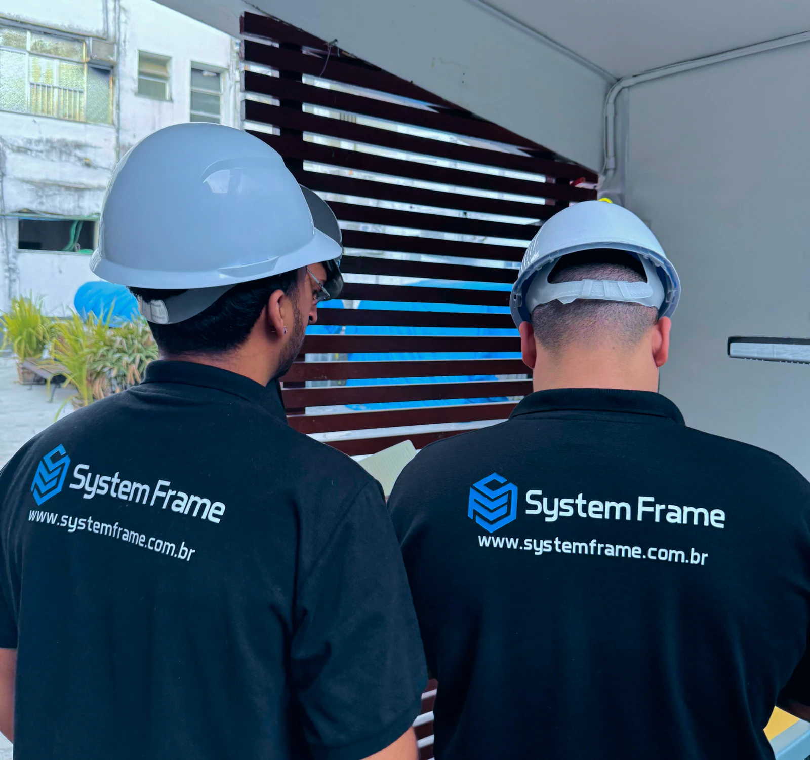 Dois profissionais de costas, com capacetes e camisetas da System Frame.