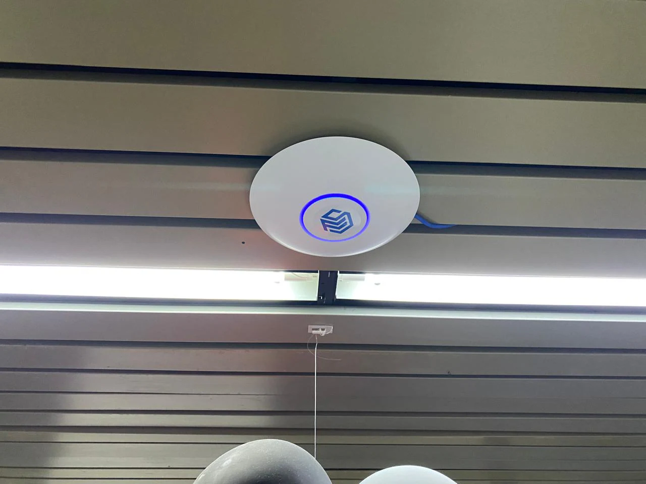 Ponto de acesso instalado sob uma viga, próximo à iluminação.